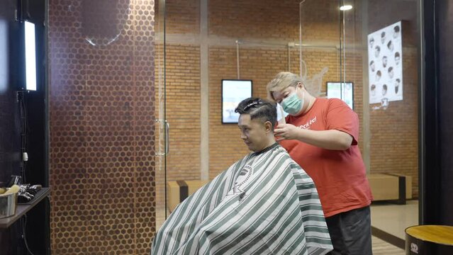 A commercial video of a barber works with hair clipper. The client getting haircut. Hands of barber with hair clipper