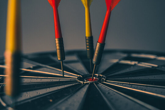 Close up shot of the dart arrow hit on bulleyes of dartboard to represent that the business reached the target of company with dark tone picture style. Target and goal as concept. 