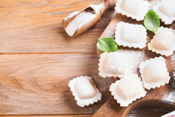 Ravioli Italian food. Tasty homemade pasta ravioli with flour, tomatoes, eggs and greens basil on wooden background. Process of making italian ravioli. Food cooking ingredients background. Top view.
