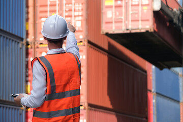 Fototapeta premium Caucasian foreman holding tablet and points his finger to control the loading position of containers.