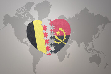 puzzle heart with the national flag of belgium and angola on a world map background.Concept.