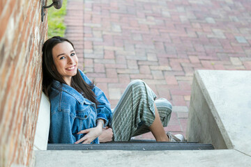 A teenage girl with long hair sitting down on some steps and looking happy