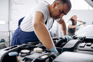 Car service mechanic worker standing in front of car engine open hood and working