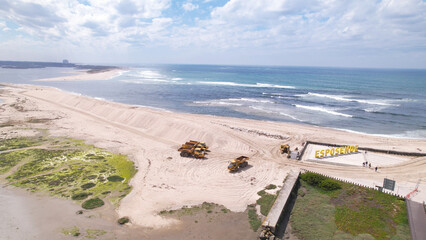 Esposende, Portugal, April 10, 2022: Aerial view of the two sides of Restinga de Ofir. Esposende fishing harbor maintenance dredging. Dumper vehicles and rotating excavator parked on the sand.