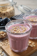 Glasses of tasty blueberry smoothie with oatmeal on wooden board, closeup