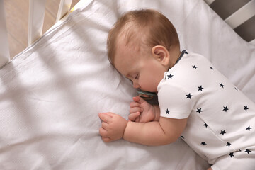 Adorable little baby with pacifier sleeping in crib, above view