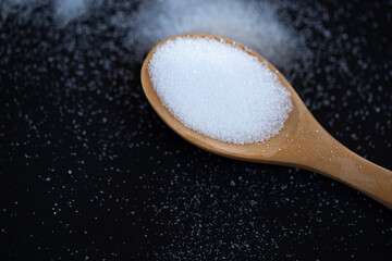 White sea salt in wooden spoon on black background. selective focus, soft picture