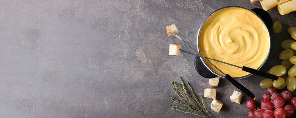 Flat lay composition with pot of delicious cheese fondue on grey table, space for text. Banner...