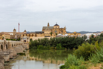 Fototapeta premium Cordoba, Spain, September 13, 2021: Guadalquivir River and the Roman Bridge, with Cordoba Mosque-Cathedral in the background.