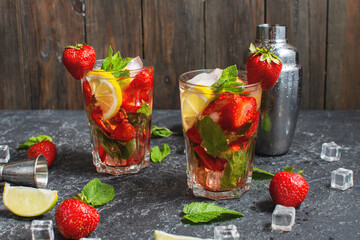 Summer refreshing mojito cocktail with strawberry, mint and lime with shaker for whipping drinks on a dark stone table