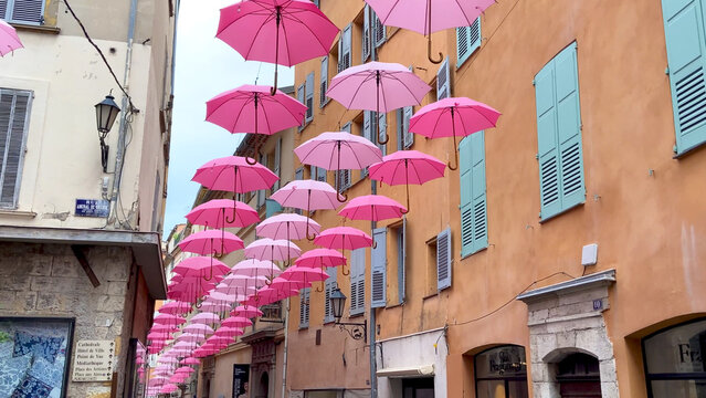Grasse,  France,  October 3, 2021: Suspended pink umbrellas in the historic center of Grasse, celebrating the Rose Expo.  Elements of architecture of Grasse with colored umbrellas between houses.