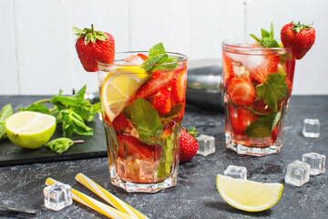 Summer refreshing mojito cocktail with strawberry, mint and lime with shaker for whipping drinks on a dark stone table