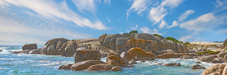 Panorama zeezicht van Camps Bay, Kaapstad, Zuid-Afrika met keien, rotsen en blauwe lucht met kopieerruimte. De golven van de oceanen spoelen aan op een ruige, rotsachtige strandkust. Reizen en toerisme in het buitenland en in het buitenland