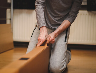 The hands of a caucasian young man open a large cardboard box in his room