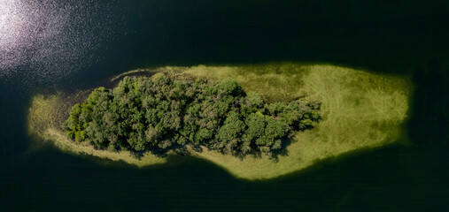 Top dow aerial panorama of green island in IJzeren Man lake full of trees with sand deposit sediment surrounding it seen just below the surface of the reflecting water