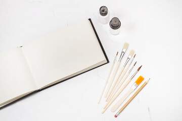 Pinceles artisticos junto a pinturas y un cuaderno para pintar sobre un fondo blanco de mármol....