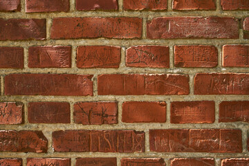 Closeup of an old red brick wall with carvings and copyspace. Zoom in on different size, shape and patterns of bricks. Details of built structure with rough surface, sketched or scratched markings