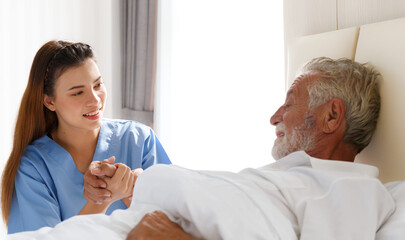 Obraz premium The young doctor held the hand of an old Caucasian man to take care of him. Talk to him from his illness lying in bed in his bedroom