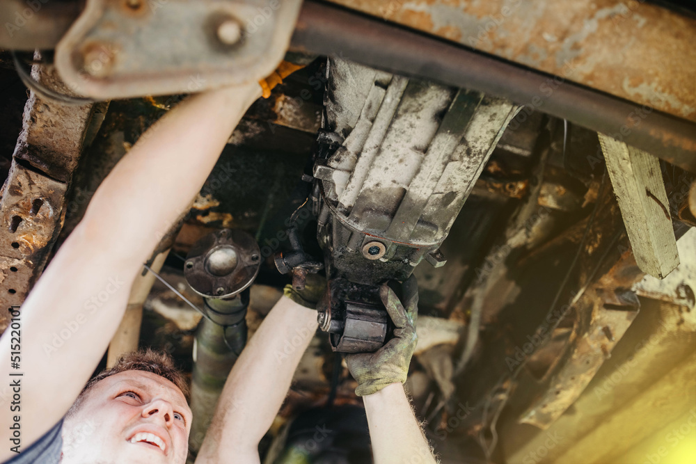 Wall mural two auto mechanic masters install a gearbox in a car. teamwork in a car service.