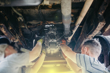 Two auto mechanic masters install a gearbox in a car. Teamwork in a car service.