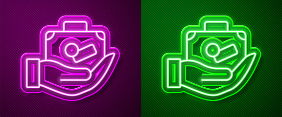 Obraz premium Glowing neon line Travel suitcase in hand icon isolated on purple and green background. Traveling baggage insurance. Security, safety, protection, protect concept. Vector