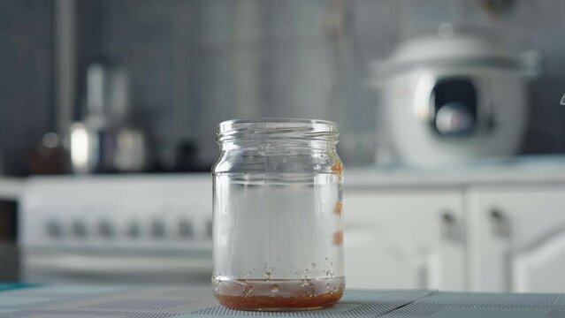 Hand with wooden spoon pours hot raspberry jam into a glass jar