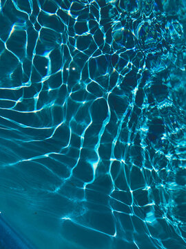 Textured vertical wallpaper from the pool. Reflection in blue pool. Water background, ripple and flow with waves. Summer blue swiming pool pattern surface. Overhead top view with place for text. 