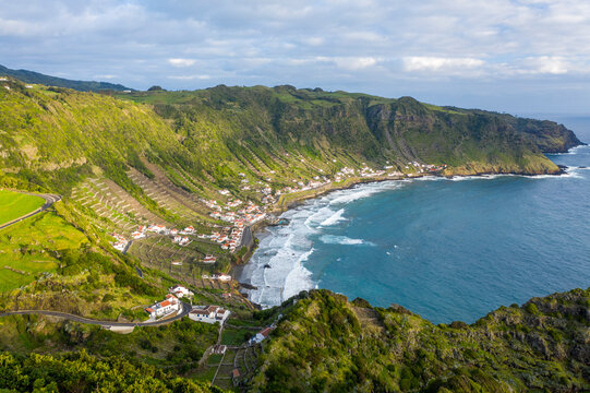 Aerial view of houses along the coastline with terrace fields on the slopes of the cliff overlooking the ocean, Santo Espirito, Azores, Portugal.