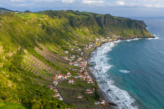 Aerial view of houses along the coastline with terrace fields on the slopes of the cliff overlooking the ocean, Santo Espirito, Azores, Portugal.