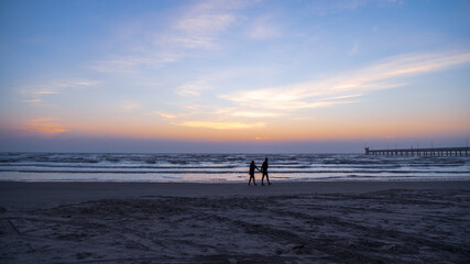 Fototapeta premium Silhouetted couple walking on the beach in the early morning just before sunrise 