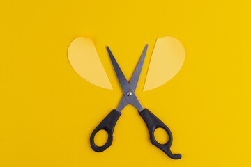 Office stationery scissors and a paper heart cut in half on pure yellow background
