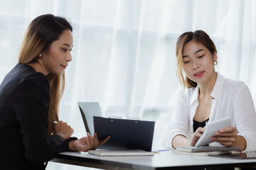 Obraz premium Atmosphere in the office of a startup company, two female employees are discussing, brainstorming ideas to working on summaries and marketing plans to increase sales and prepare reports to managers.