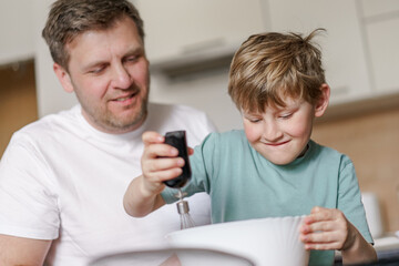 Dad and little son baking together in kitchen, preparing dough for pie, having fun at home, preparing a surprise for mom on mother's day