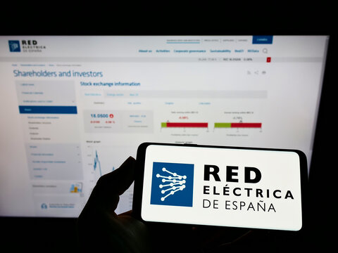 Stuttgart, Germany - 01-30-2022: Person holding mobile phone with logo of Spanish energy company Red Electrica de Espana on screen in front of web page. Focus on phone display.