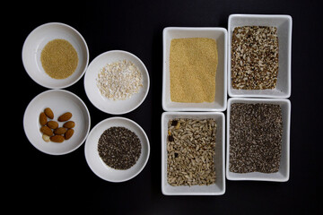 Dark background with white bowls contain healthy seeds for a vegan diet