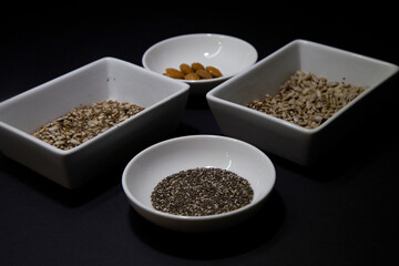 Almonds, chia and other healthy vegan seeds in white porcelain bowls on a black background