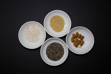 Almonds, chia and other healthy vegan seeds in 4 round white porcelain bowls on a black background