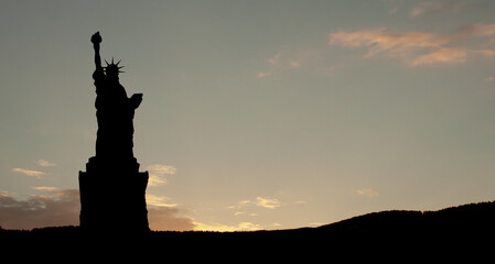 Fototapeta premium Silhouettes of The Statue of Liberty at sunset. Greeting card for Independence Day.
