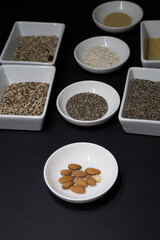 Almonds, chia and other healthy vegan seeds in white porcelain bowls on a black background