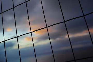 Closeup of a wire fence at sunset. Background of vertical and horizontal lines. Silhouette of wire mesh in rectangle shapes for security concept.