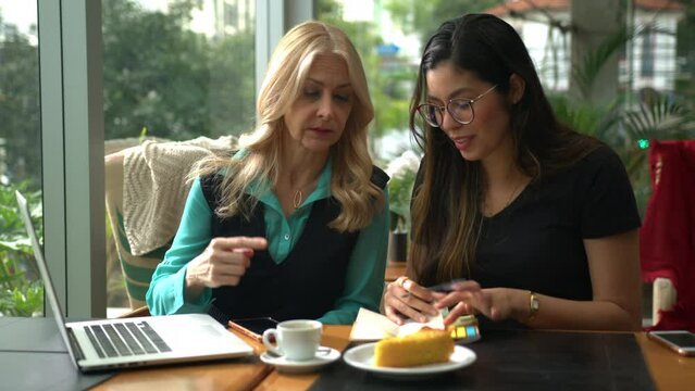 Older executive woman mentoring younger female colleague. Young woman taking notes listening to senior leader at coffee shop