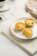 Traditional portuguese vanilla pudding puff pastry pastel de nata on white plate on marble board with a cup of coffee in white porcelain