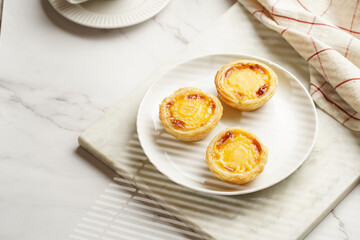 Traditional portuguese vanilla pudding puff pastry pastel de nata on white plate on marble board with a cup of coffee in white porcelain