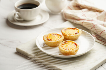 Traditional portuguese vanilla pudding puff pastry pastel de nata on white plate on marble board with a cup of coffee in white porcelain