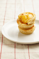 Traditional portuguese vanilla pudding puff pastry pastel de nata stacked on each other on white plate on checkered table cloth