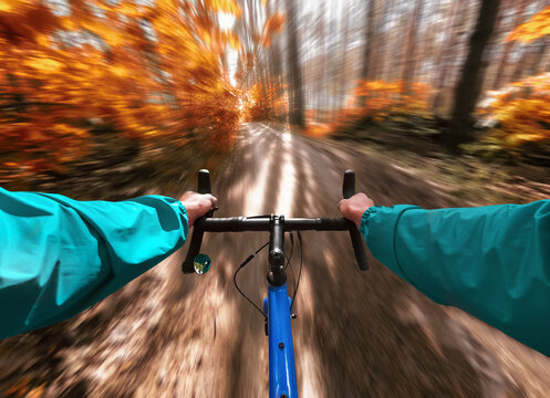 Cyclist rides gravel bike on a trail in the autumn forest. Motion blur effect. First-person view.
