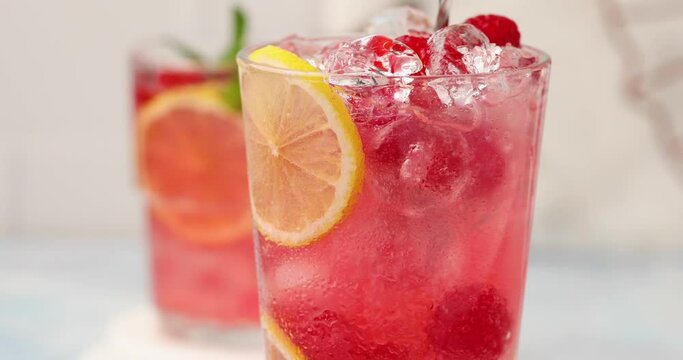Spring or summer refreshing cold cocktail or mocktail with berries and lemon, raspberry lemonade being stirred with a spoon