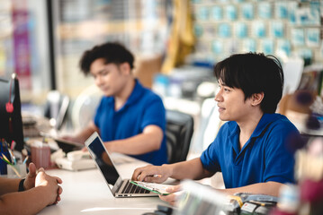 Young male worker focused on working on laptop in a car shop with NFC payment machine on desk to receive card payment