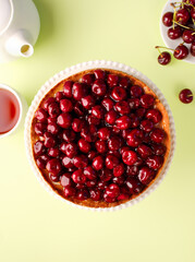 An open cherry pie on the kitchen table, on a cake pan, on a colored green background. Fruit cake. Tart. Cherry pastries with fresh berries. Summer berry vegan pie. Top view, copy space, close up.