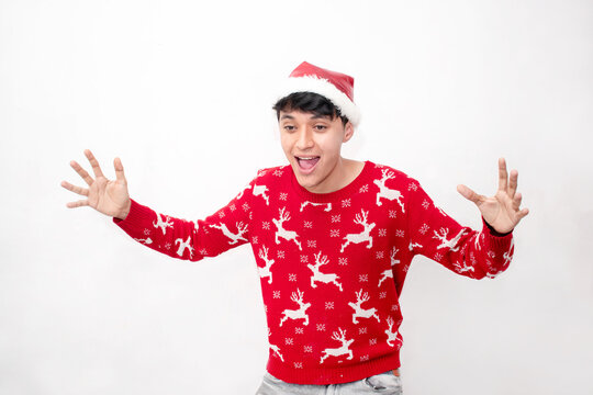 Joven hombre sorprendido y feliz con los brazos extendidos con ropa navideña en un fondo blanco aislado 